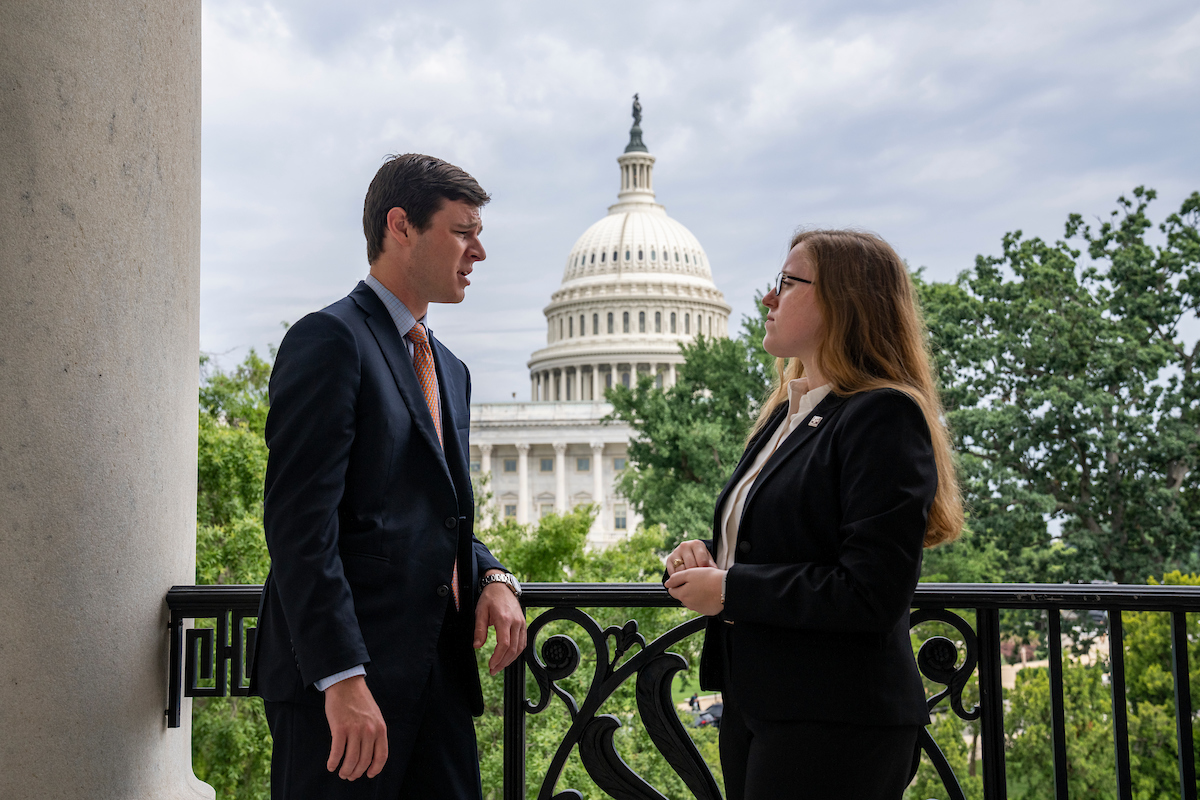 Two students standing on balcony with US Capitol in the background.